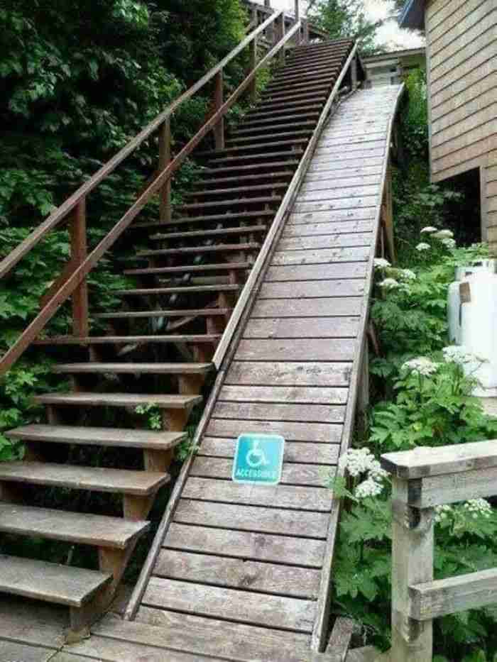 Image of a very long, steep wooden set of stairs. Directly next to it is an equally long, steep wooden ramp with an accessibility symbol on it.