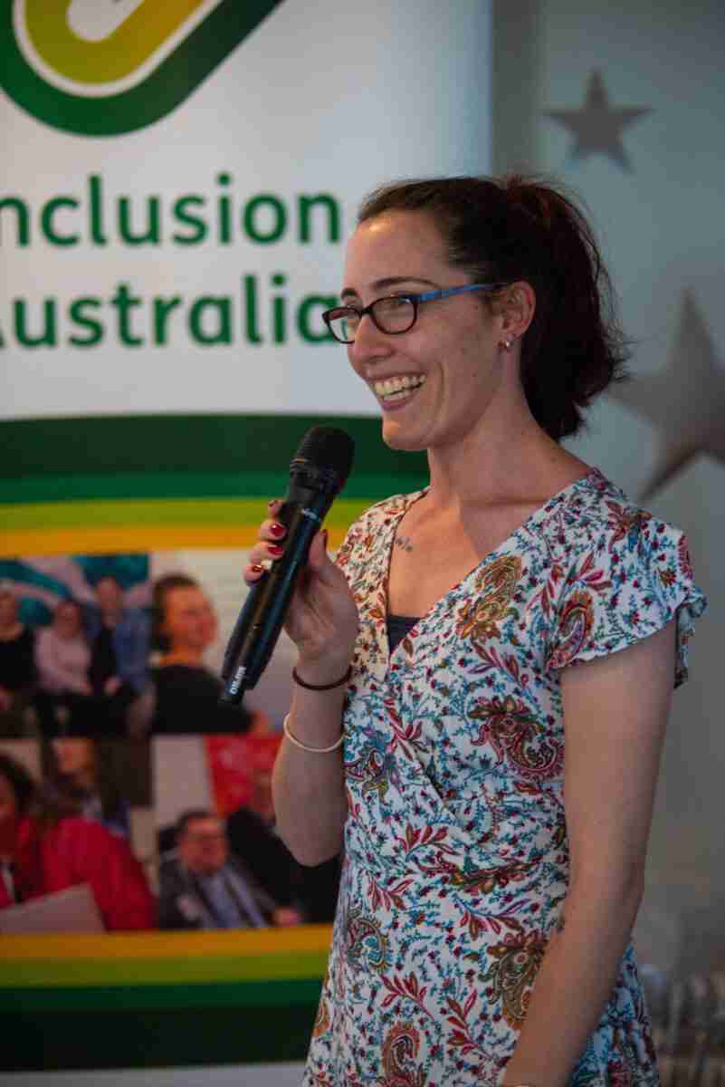 Person presenting in front of a sign that says Inclusion Australia