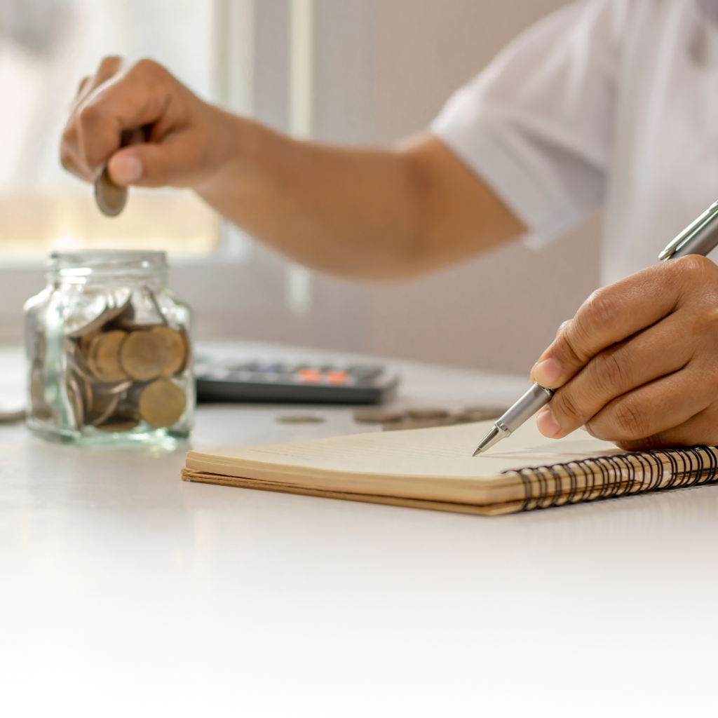 Image of a person dropping a coin into a jar while using the other hand to write in a notebook