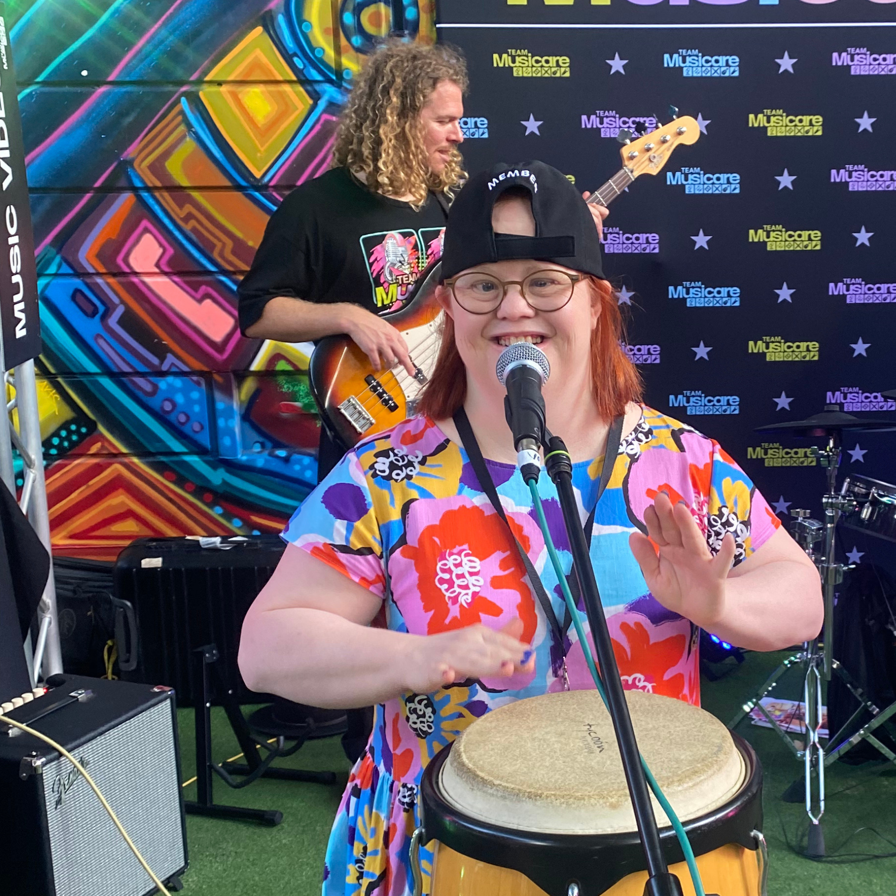 A lady with Down Syndrome wearing colourful clothes, banging a drum