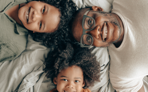 A man and two kids laying on a bed smiling up at the camera