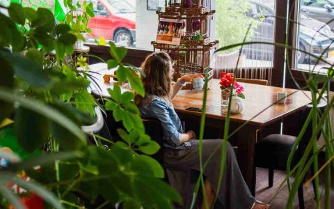A woman sitting at a table in a cafe drinking from a mug