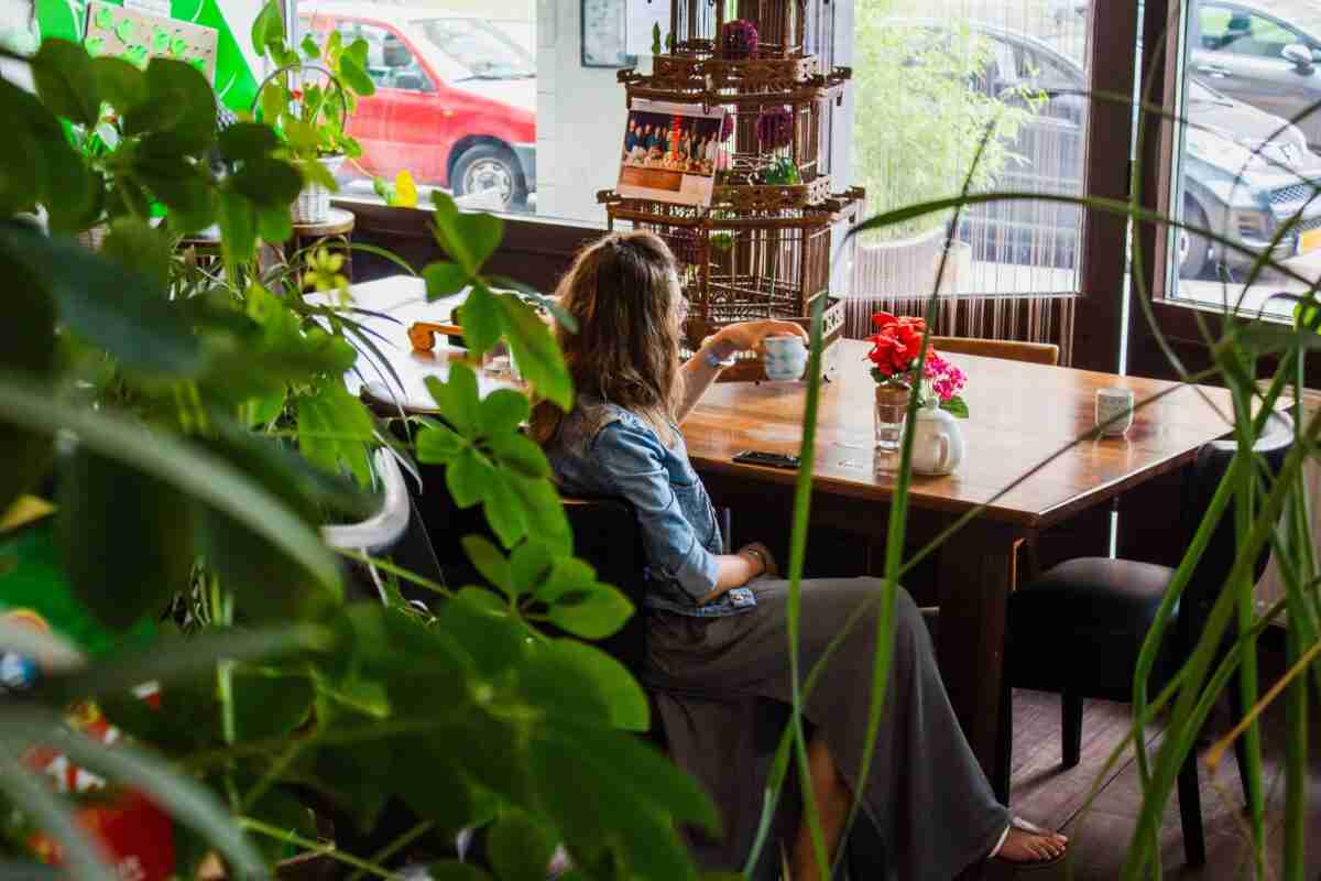 A woman sitting at a table in a cafe drinking from a mug