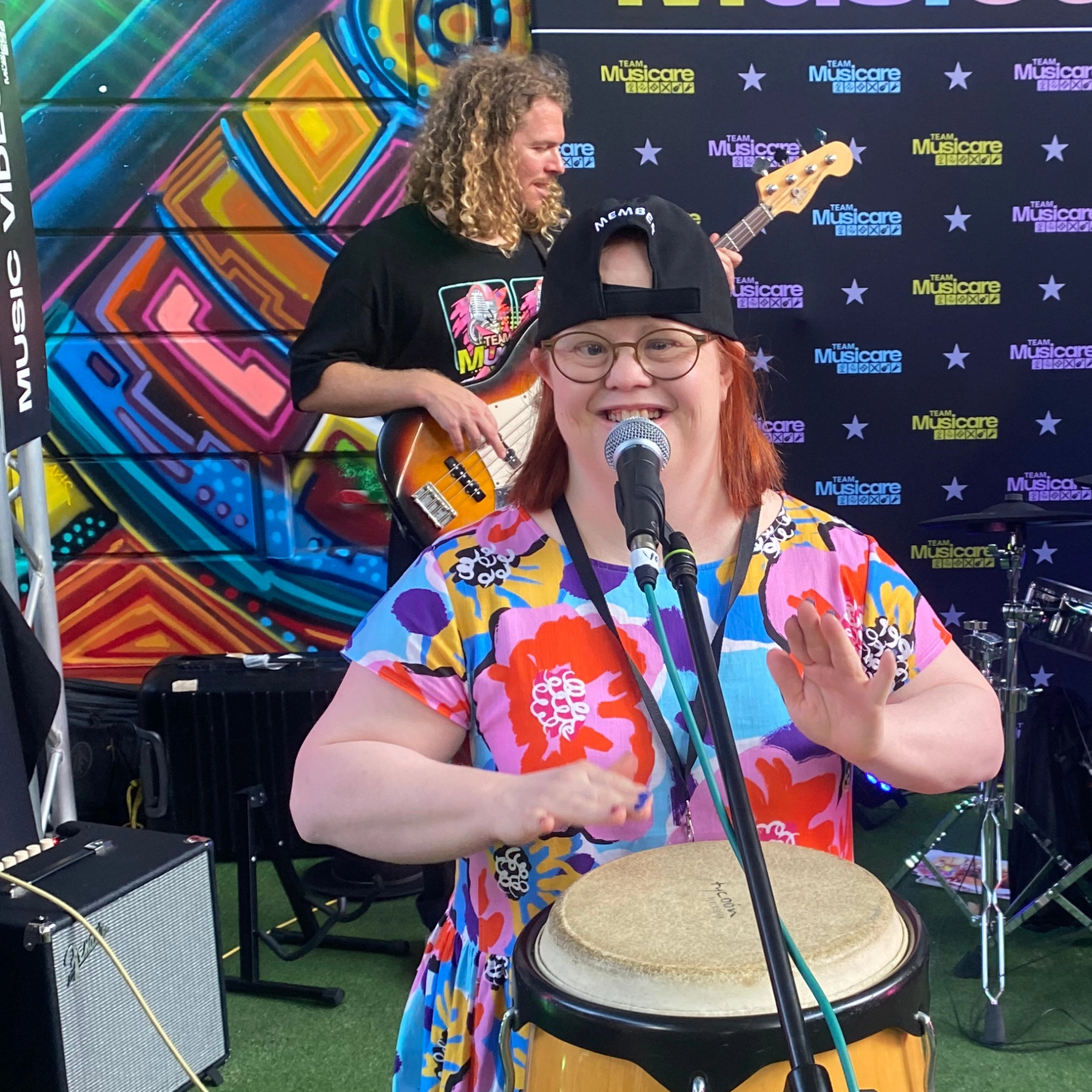 A lady with Down Syndrome wearing colourful clothes, banging a drum