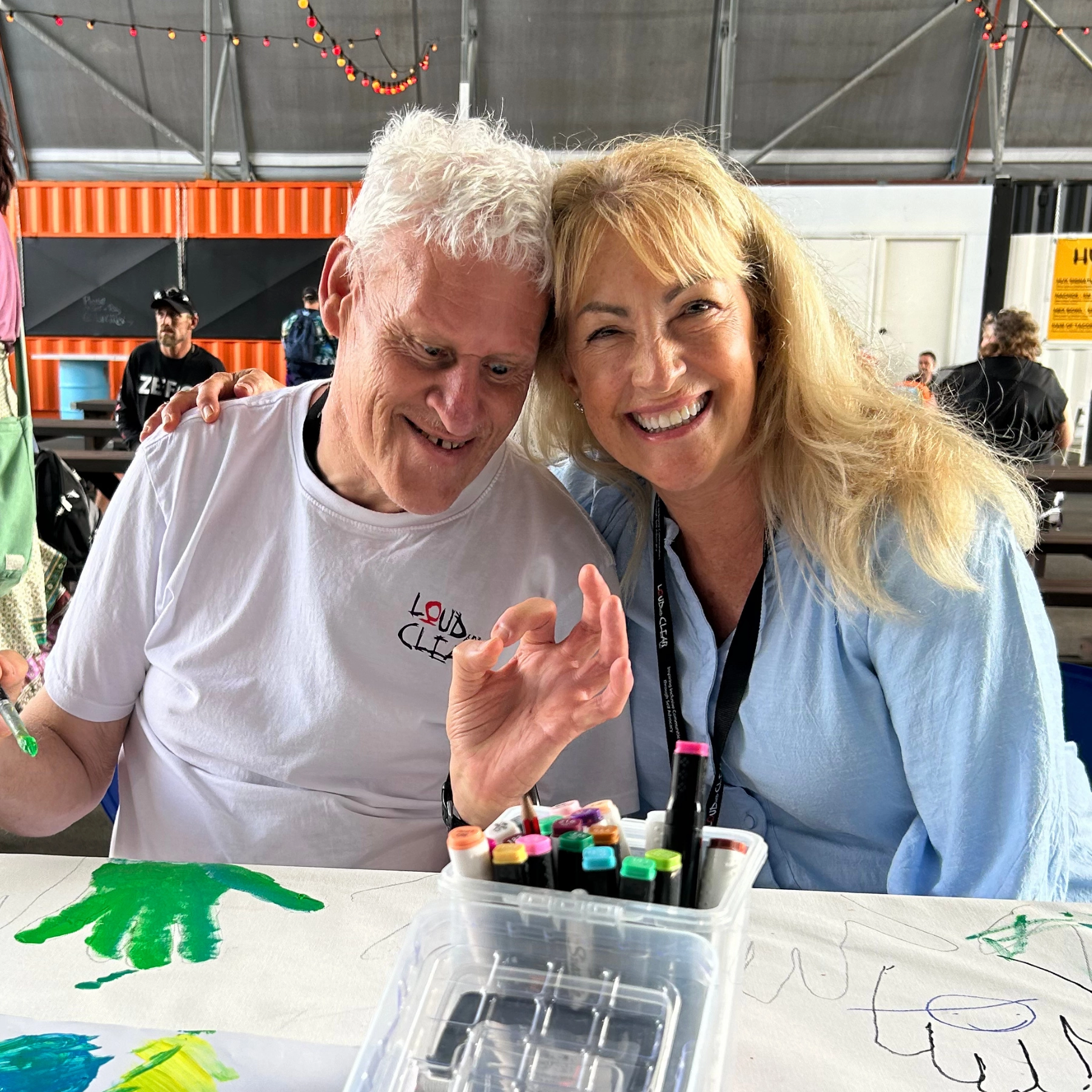 A man smiling making an OK symbol with his hand and a smiling woman with arm over his shoulders