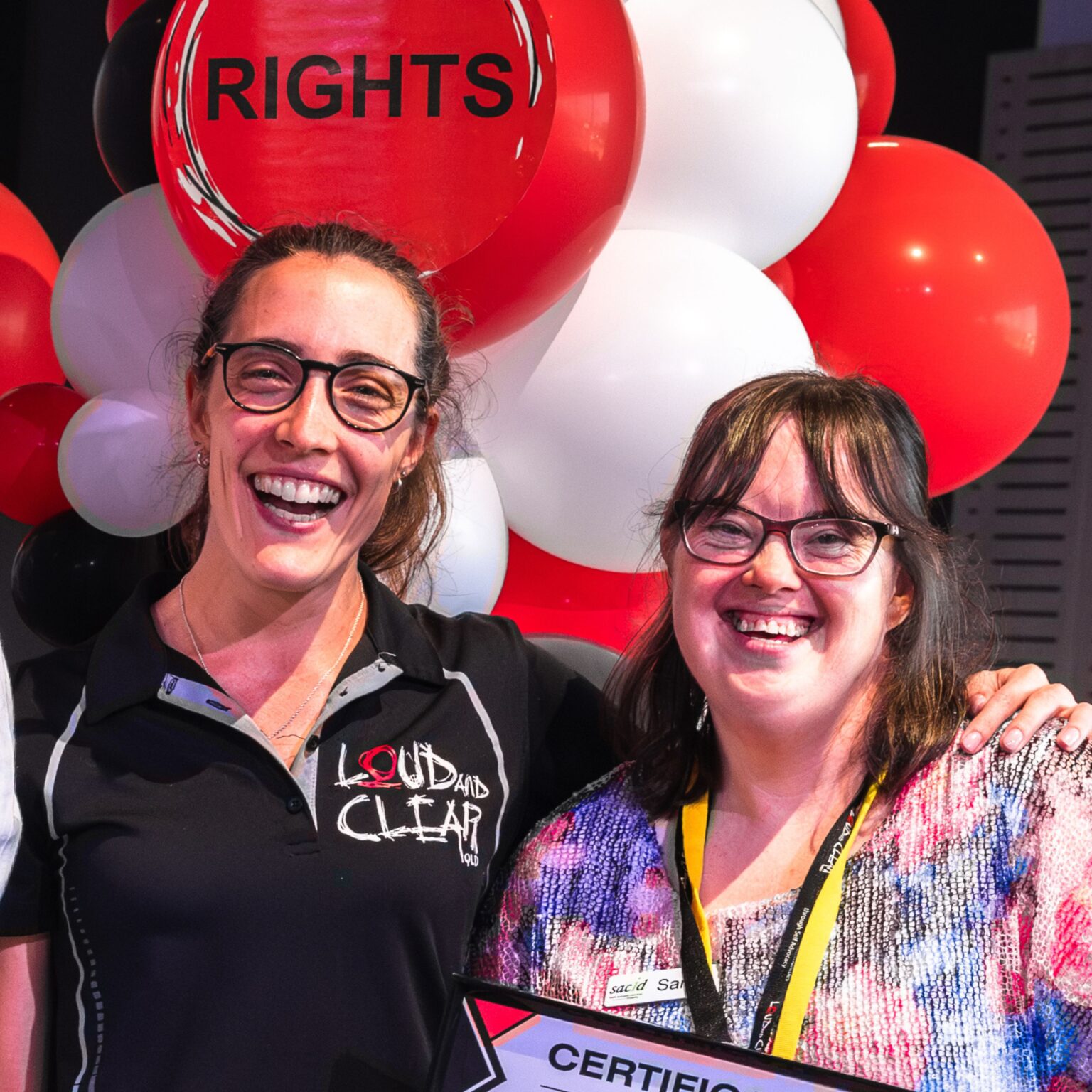 Two women laughing standing in front of red and white balloons